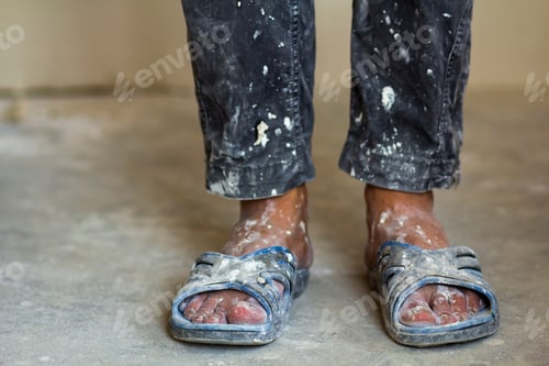 Preview: Feet of a construction worker in old dirty clothes and shoes