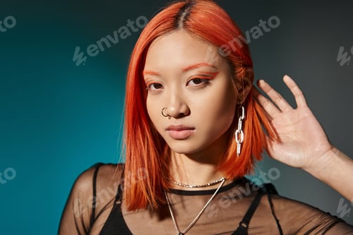 Preview: portrait of pierced asian woman with bold eye makeup and trendy earring on blue background
