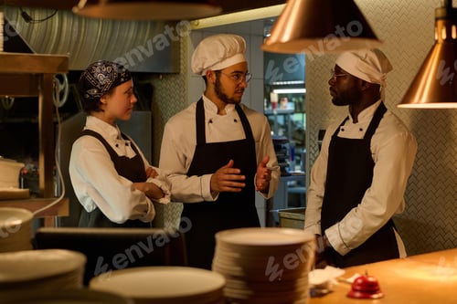 Preview: Three young intercultural cooks in uniform discussing working points