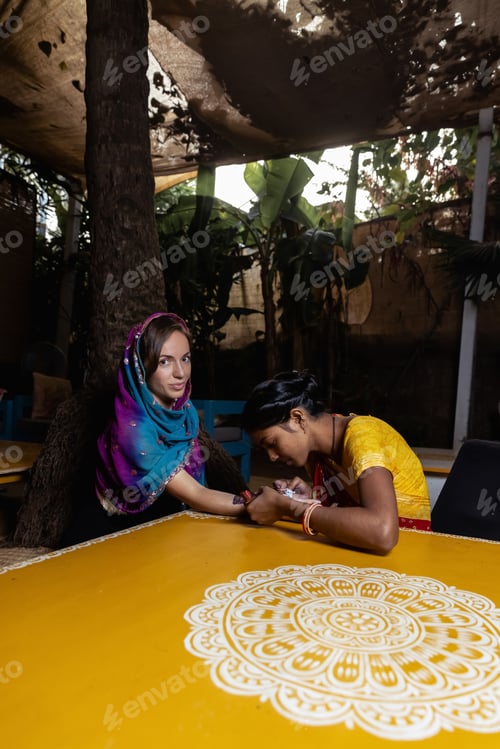Preview: Indian artisan is applying mehndi on the hands of a bride wearing a saree