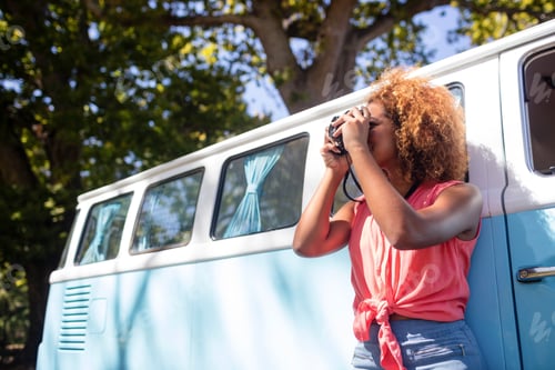 Preview: Woman leaning on campervan and photographing with camera