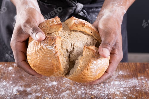 Preview: Midsection of african american male baker breaking bread over table