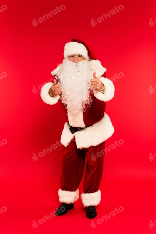 Preview: Santa claus in eyeglasses showing like gesture at camera on red background
