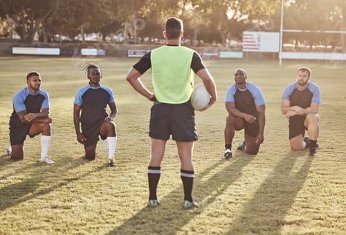Preview: Rearview rugby coach talking to and addressing his players during a practice session outside on a f