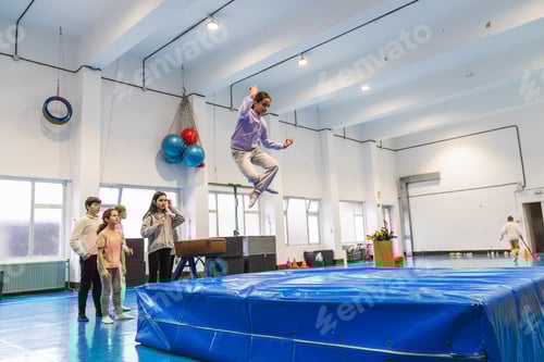 Preview: Teenage girl practicing gymnastics jumping on blue mat in school gym
