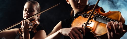 Preview: attractive musicians playing on violins on dark stage with smoke, website header