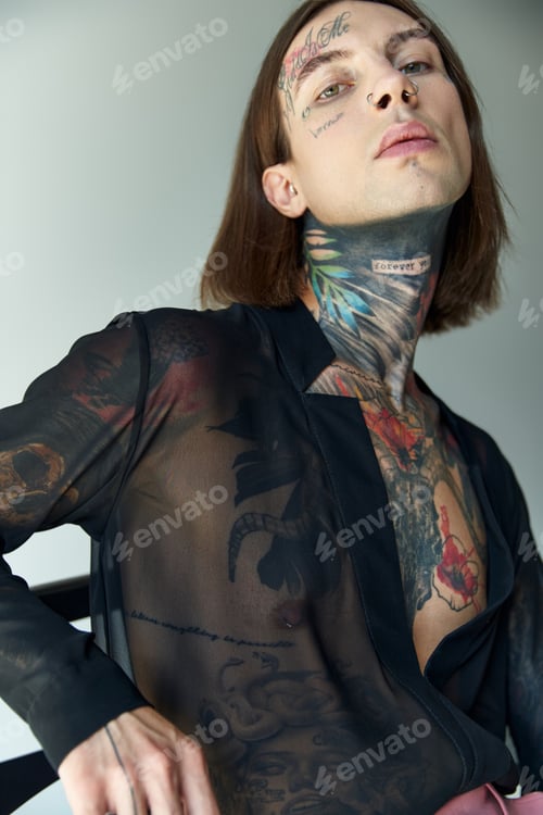 Preview: vertical shot of handsome young man with tattoos and piercing in black transparent blouse, fashion
