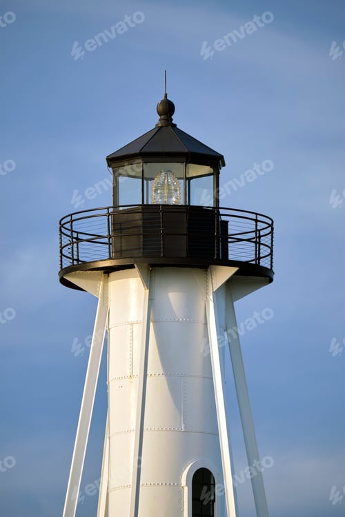 Preview: White tall lighthouse on sea shore against blue sky for commercial vessels navigation