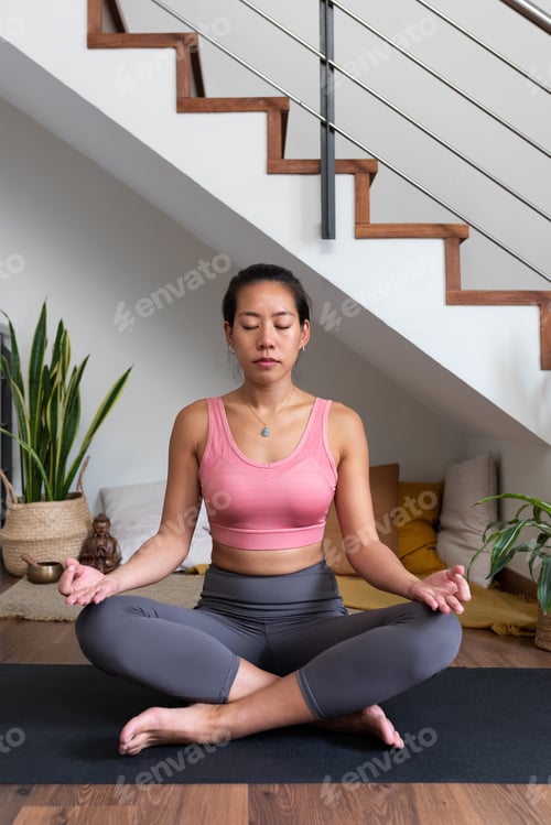 Preview: Vertical portrait of Asian woman meditating at home sitting on yoga mat.Spirituality and mindfulness