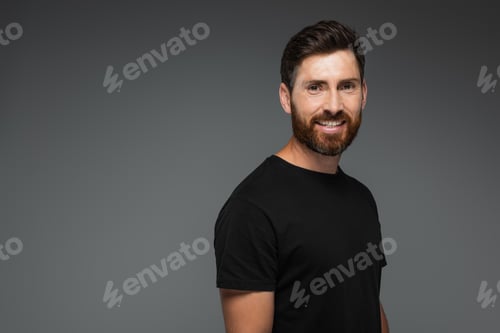 Preview: portrait of smiling bearded man in black t-shirt looking at camera isolated on grey
