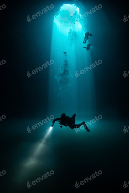 Preview: Divers exploring the mysterious depths of an underwater cave illuminated by a shaft of light.
