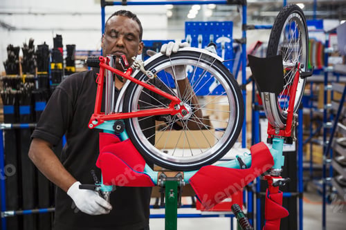 Preview: Male skilled factory worker assembling a bicycle in a factory, attaching a wheel.