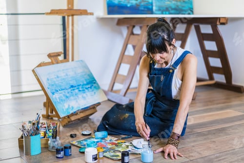 Preview: Woman artist painting on a canvas a blue abstract painting.