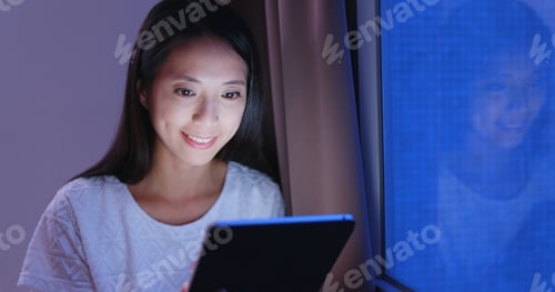 Preview: Woman looking at tablet computer in the evening