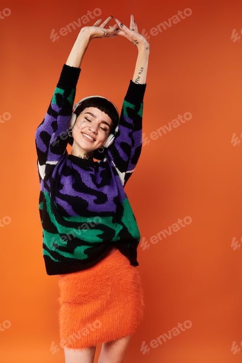 Preview: Young woman with short hair and tattoos happily posing in a colorful sweater