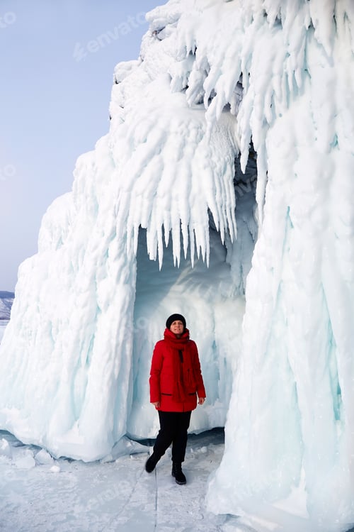 Preview: A woman stands by a rock covered with snow and huge icicles.