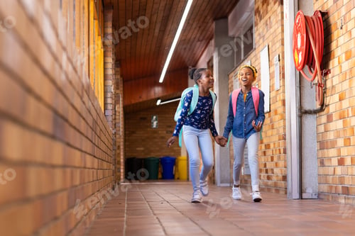 Preview: Walking in school hallway, two african american girls with backpacks smiling and holding hands