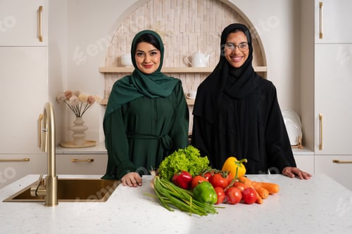 Preview: Emirati women in traditional abayas preparing healthy meal in modern kitchen