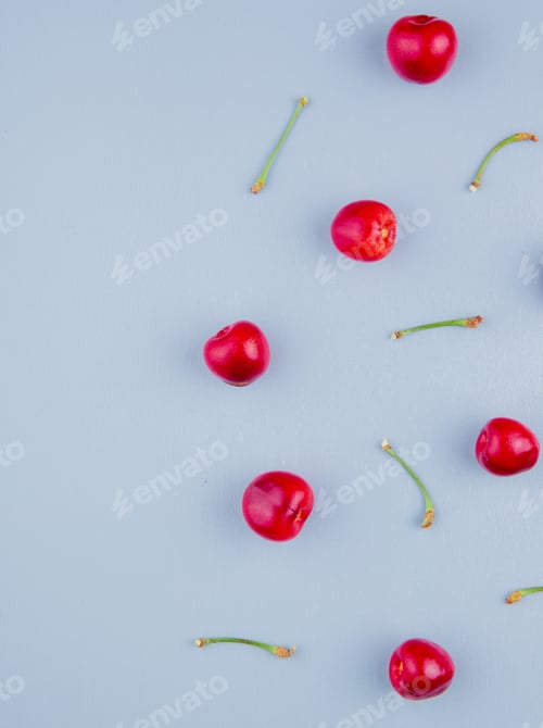 Preview: top view of red cherries with stems on blue background