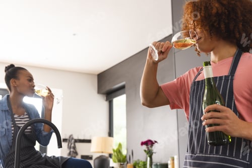 Preview: Happy diverse couple preparing meal drinking wine in sunny kitchen