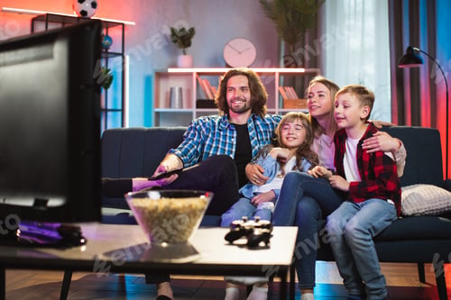 Preview: Friendly family, sitting on the sofa at home in the evening, watching TV and having fun