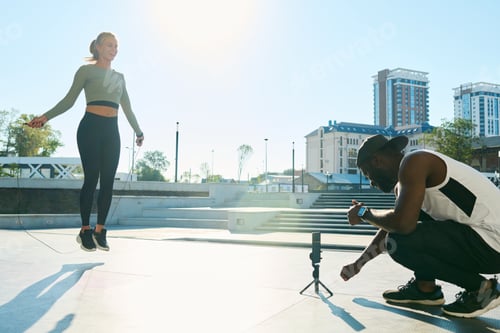 Preview: Happy young woman jumping over skipping rope while man shooting video