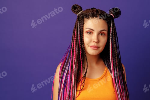 Preview: Smiling positive young woman with colorful african braids on purple background