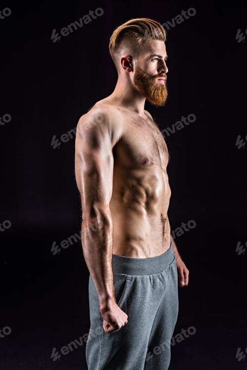 Preview: handsome bearded sportsman posing and standing isolated on black in studio