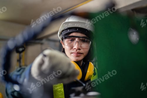 Preview: A woman in a yellow vest and a hard hat is working on a machine