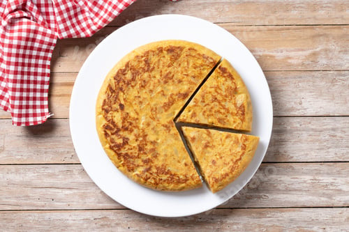 Preview: Traditional spanish omelette with ingredients on wooden table.