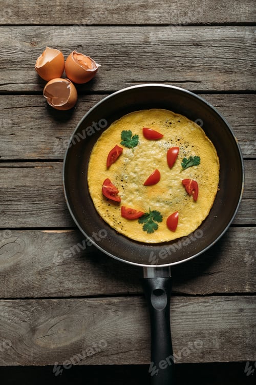 Preview: top view of fresh omelet with vegetables in frying pan on wooden table