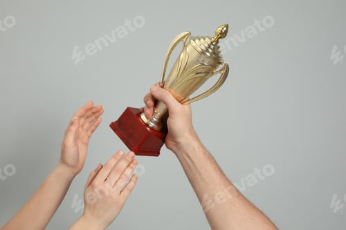 Preview: People with gold trophy cup on light grey background, closeup