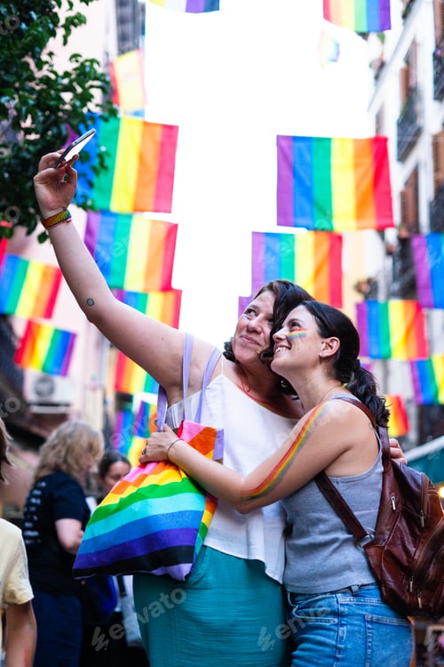 Preview: Two lesbian women taking a selfie at gay pride parade with rainbow flags