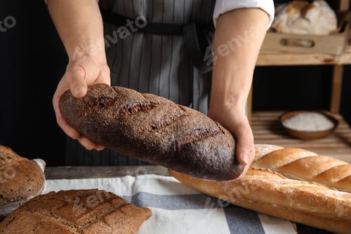 Preview: Baker holding loaf of bread over table indoors, closeup