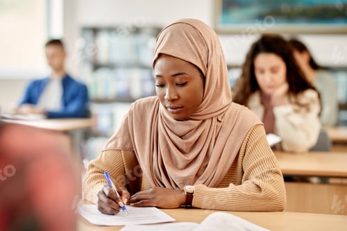 Preview: Black Muslim woman writing an exam in the classroom at the university.