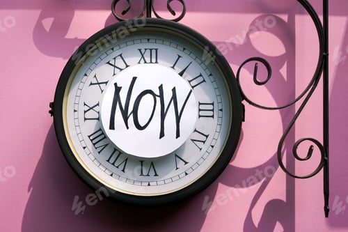 Preview: When the time is right. Flat lay traditional clock on the pink background with the words 'Now'.