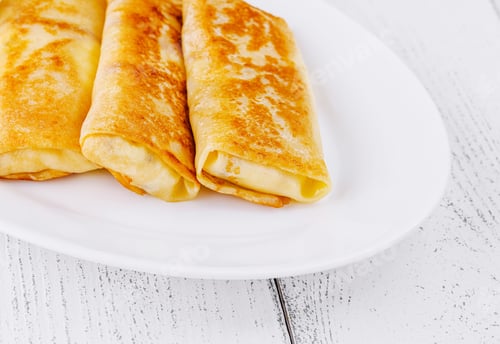 Preview: Thin pancakes with filling lying on white plate on wooden table