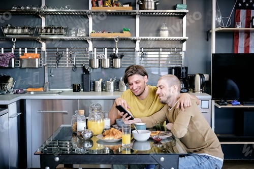 Preview: Two men scrolling in smartphone over kitchen table