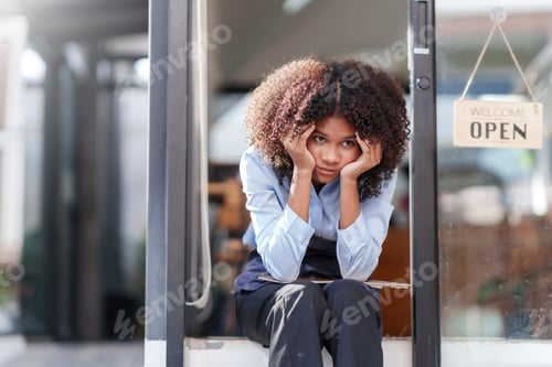 Preview: Female shopkeeper sitting stressed out at the store entrance frustrated by the economic impact.