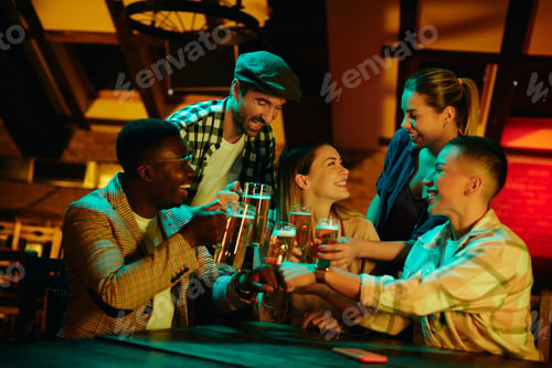 Preview: Young happy adults having fun while drinking beer and toasting in a bar.