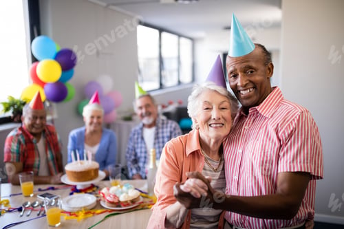 Preview: Portrait of senior couple wearing party hats standing by table