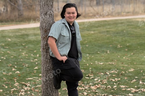 Preview: Cheerful young man is standing next to a tree trunk and smiling