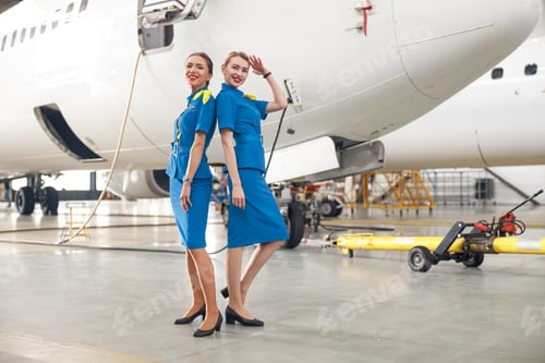 Preview: Full length shot of two pretty air stewardesses in bright blue uniform smiling at camera