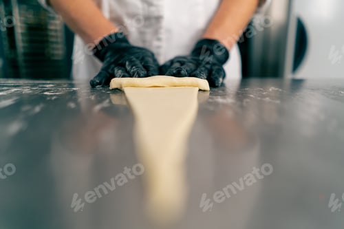 Preview: Close-up chef's gloved hands shaping and twisting raw dough into the shape of croissants for baking