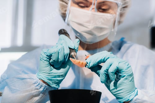 Preview: A masked and gloved dental technician works on a prosthetic tooth in his lab