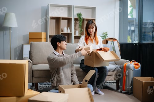 Preview: Young couple preparing for a move, packing boxes and a suitcase in a cozy living room. Perfect for