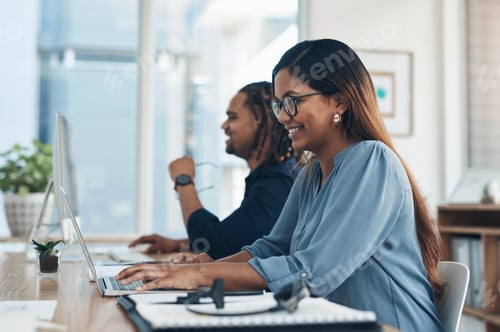 Preview: Shot of a young businesswoman working on a laptop in an office with her colleague in the background