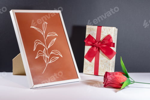 Preview: Closeup of a small jewellery gift box with an artificial rose and a photo frame on the table