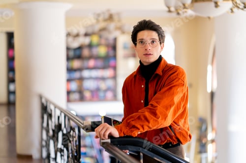 Preview: portrait of a young guy in glasses standing with a book in his hands in library