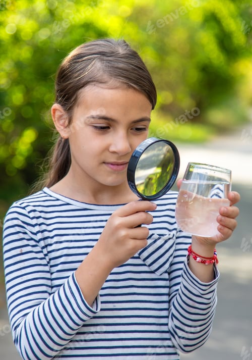 Preview: The child examines the water with a magnifying glass. Selective focus.